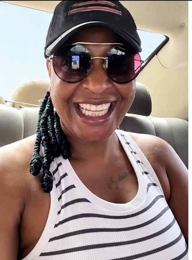 Doris Ogala in a cap, sunglasses and striped top smiling during a video call in a car