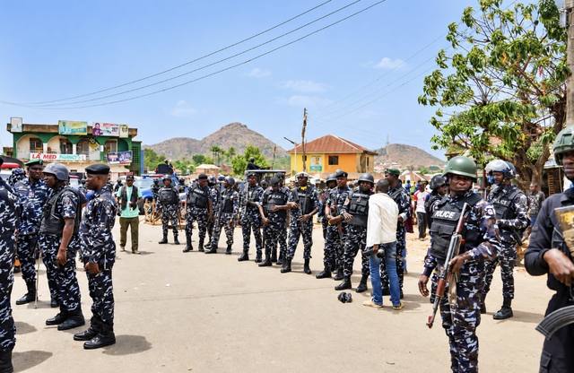 Armed police officers in helmets and vests line a street in a Nigerian town
