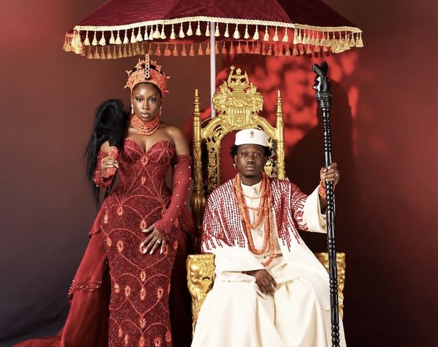 Davita Lamai in a red beaded gown and coral crown stands beside Zlatan, seated on a gold throne in white and coral beads